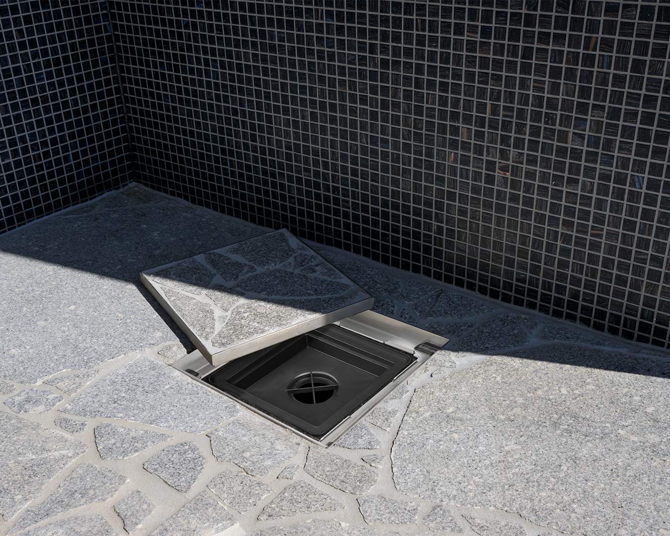 HIDE Hidden Drain Covers with grey stone crazy pave inlay open to view traditional black plastic drain grate underneath.