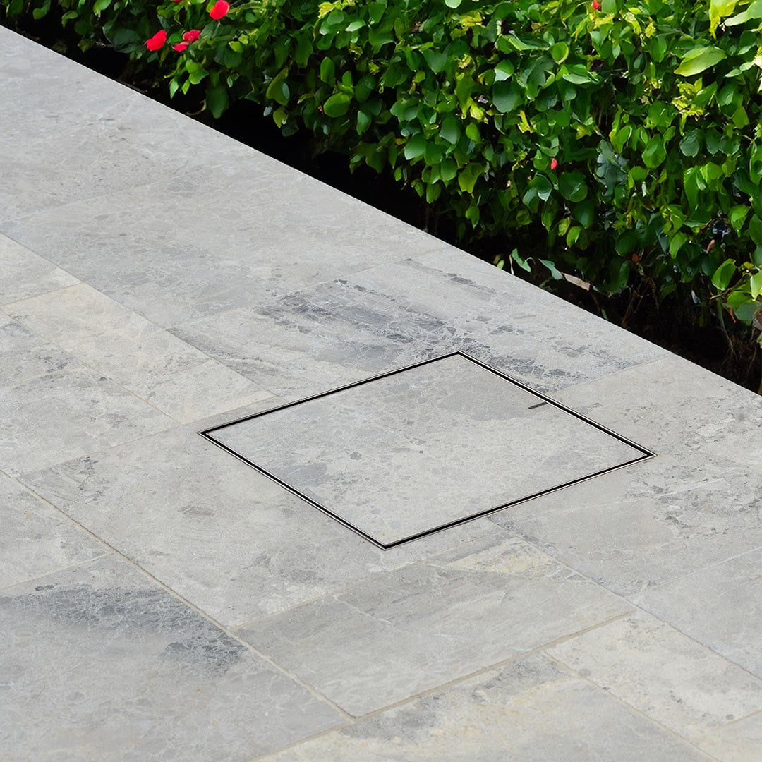 HIDE Hidden Drain Covers with grey tile and green bushes in the background.
