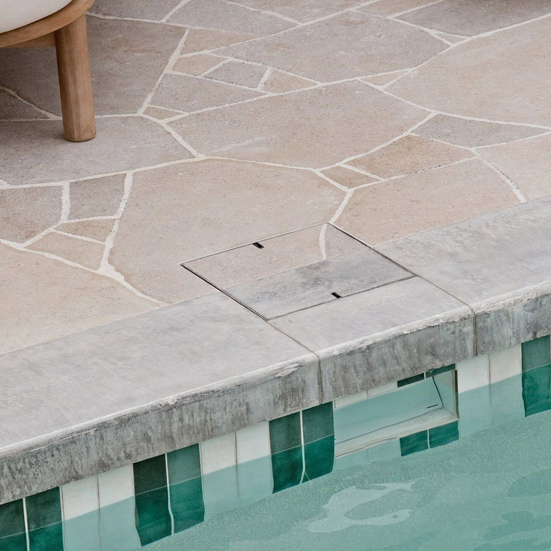 HIDE stainless steel Skimmer Cover with dual concrete and crazy pave inlay set flush in pool coping, with stone inlay blending into the crazy paving and joint lines continuing through the lid.