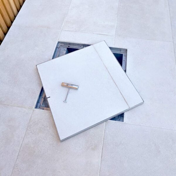 Large Stainless Steel HIDE Manhole Cover with white tile inlay, sitting open to view service access point underneath.
