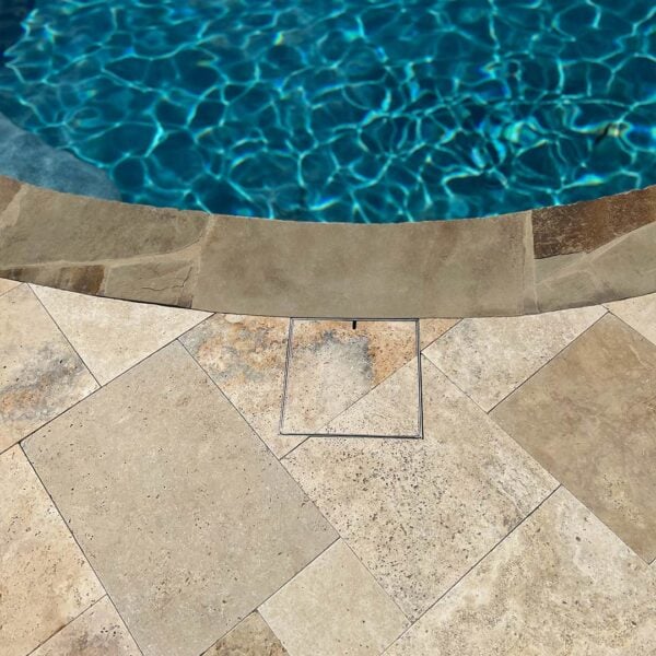 HIDE stainless steel skimmer cover set flush in stone paving at the pool edge; grout lines continue through the cover to maintain the surrounding pattern.
