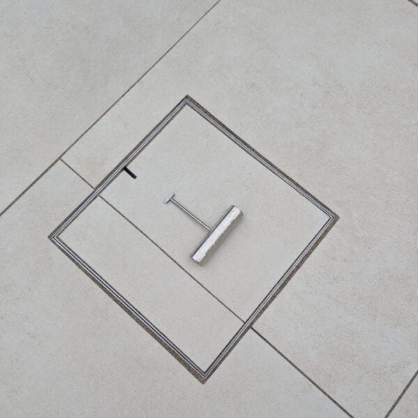 HIDE Access cover with grout running through grey paving with HIDE safety key laying on top.