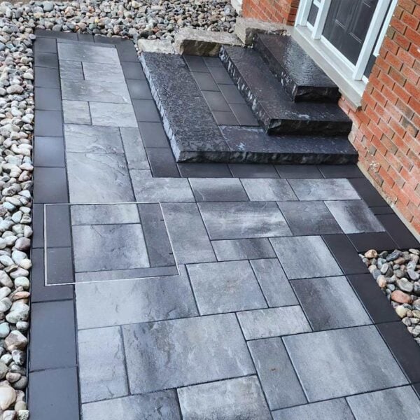 Large HIDE stainless steel access cover set flush in two-tone paver walkway; joint lines align to continue the surrounding paving layout.