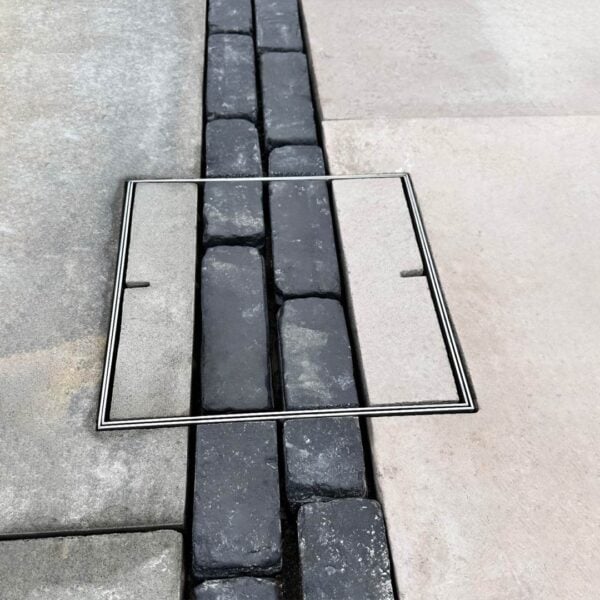 Stainless Steel HIDE Access Cover with paving inlay. Close up view with black pacing patten continuing through the HIDE Cover to create a seamless hardscape design.