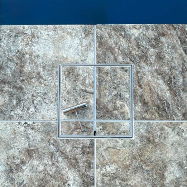 HIDE stainless steel Skimmer Cover with stone tile inlay; grout pattern cross the lid to match the surrounding paving, with lifting safety key shown.