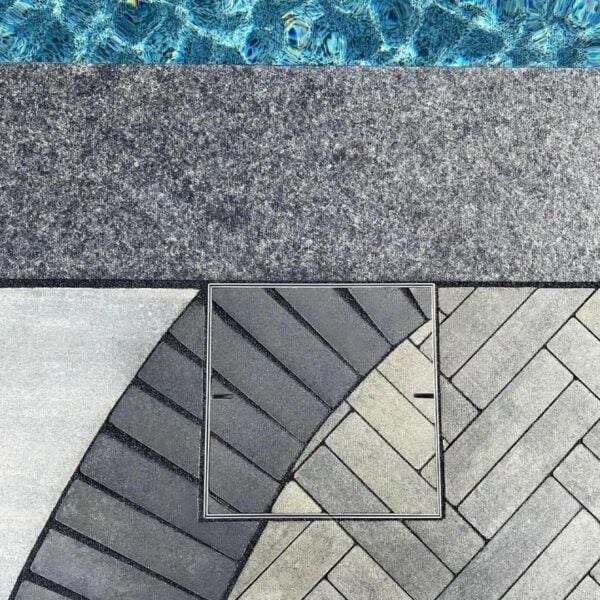 HIDE stainless steel skimmer cover inlaid with curved and herringbone pavers; joint lines flow through the lid to preserve the poolside pattern.