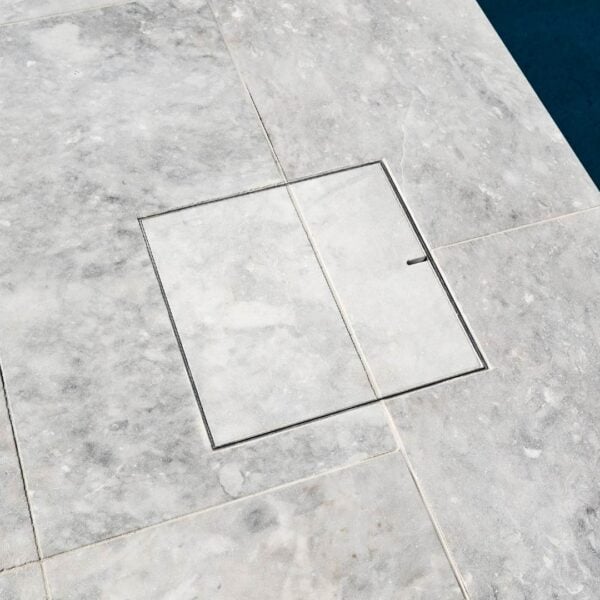 HIDE stainless steel Skimmer Cover with stone tile inlay set flush beside the pool; grout line continues through the cover for a seamless finish.