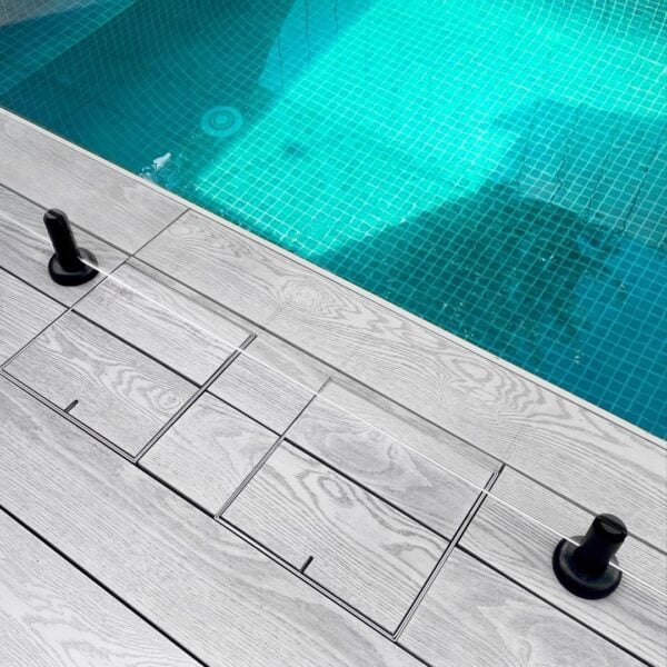 Two HIDE stainless steel Skimmer Covers sitting flush in timber decking beside the pool; board joints align through the cover to continue the deck pattern.
