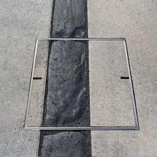 HIDE stainless steel Access Cover installed flush in concrete pavers, centred over a contrasting strip with paving pattern lines aligned.