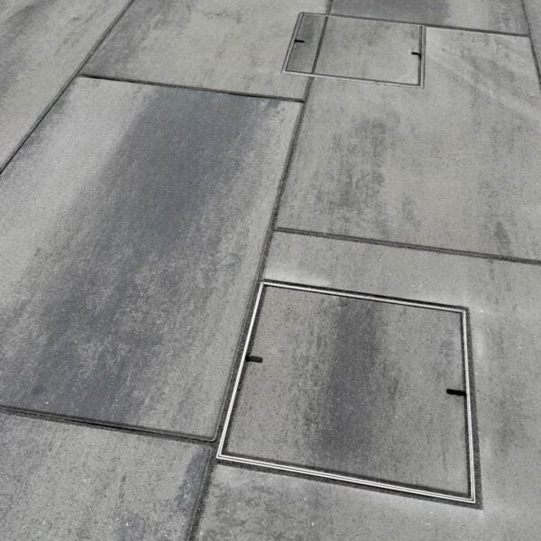 Two HIDE stainless steel Access Covers set flush in stone paving; grout lines align through each cover to continue the surrounding tile pattern.