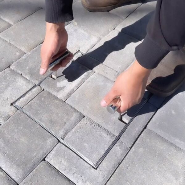 HIDE stainless steel skimmer cover being lifted up with the HIDE Safety Key, showing flush inlay installation with paving pattern aligned to following surrounding hardscape.