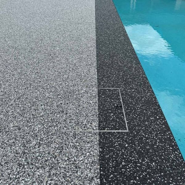 HIDE stainless steel skimmer cover set flush in permeable paving beside the pool, blending into the two-tone aggregate surface.