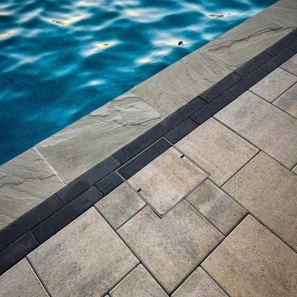 HIDE Stainless Steel Skimmer Cover with dual black and grey paving inlay continuing the surrounding paving pattern.