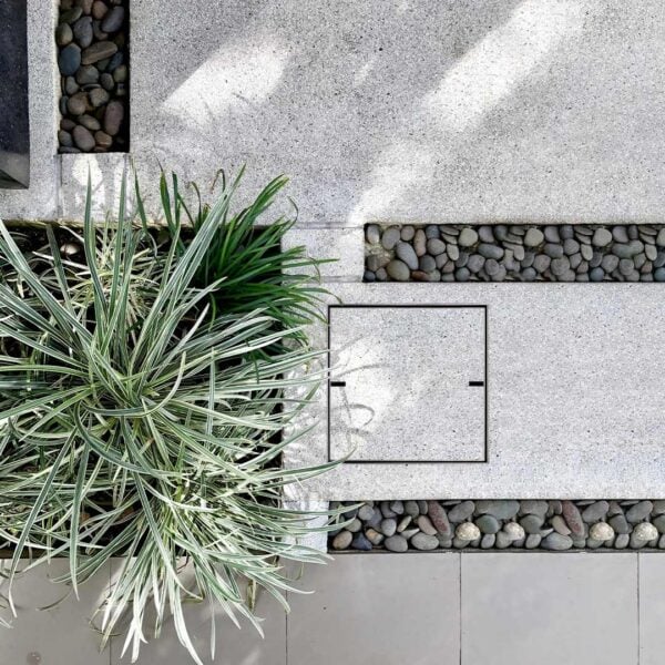 Stainless Steel HIDE Drain Cover installed in grey exposed aggregate concrete footpath.
