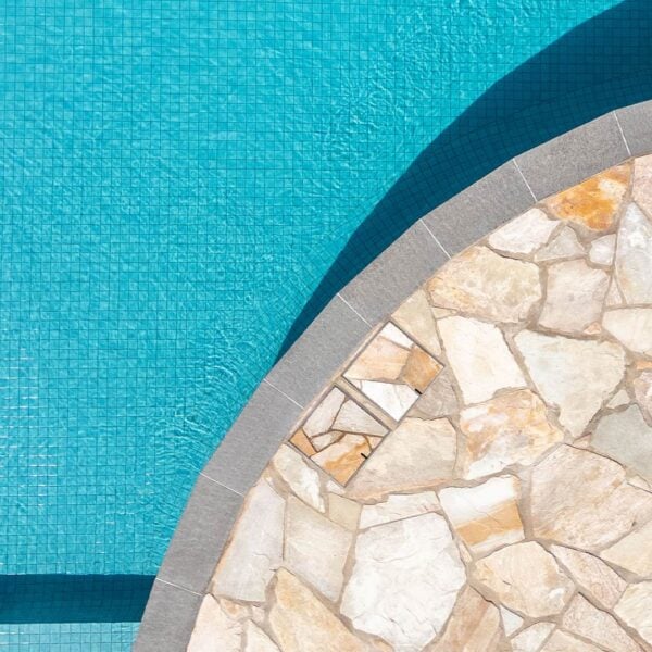 Tope view of two HIDE Skimmer Cover with cream orange crazy pave pattern around curved pool.