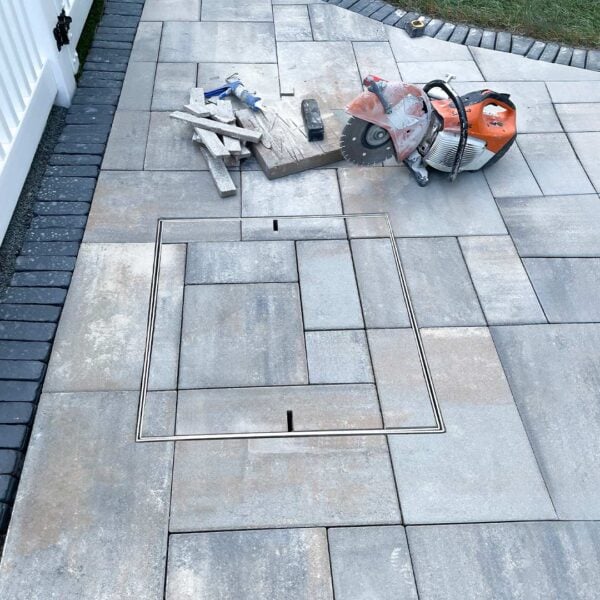 HIDE Manhole Cover with blue grey paving inlay installed into backyard paving.