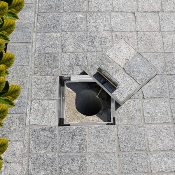 Small 156mm HIDE Access Cover with grey stone paving inlay sitting open to view service access pipe underneath.