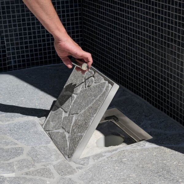 HIDE Drain Cover with crazy pave inlay being opened to show drain pipe underneath cover.
