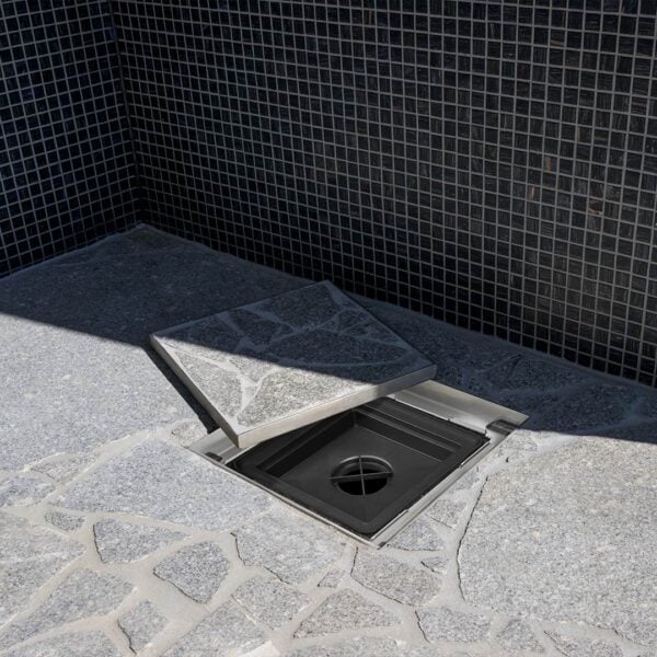 Stainless Steel HIDE Hidden Drain Covers with crazy pave inlay sitting open to reveal plastic drain grate underneath showing a before and after view.